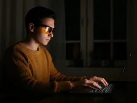 Person med gule blålysbriller bruker laptop om natten i mørkt rom