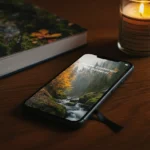 Telefon med skjermen ned på trebord med naturbok og stearinlys