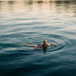Norsk kvinne svømmer i krystallklart fjordvann på sommerkveld med gyllent lys