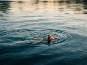 Norsk kvinne svømmer i krystallklart fjordvann på sommerkveld med gyllent lys