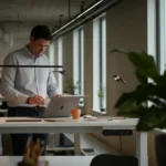 Norsk kontorarbeider ved hevsenk skrivebord i lyst moderne nordisk kontor
