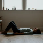 Person i savasana posisjon på yogamatte i fredelig skandinavisk rom med mykt lys