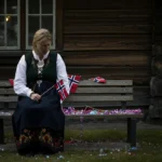 Sliten forelder i bunad sitter alene på en benk om kvelden, et bilde på 17 mai tretthet