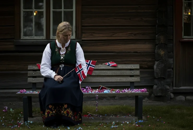 Sliten forelder i bunad sitter alene på en benk om kvelden, et bilde på 17 mai tretthet