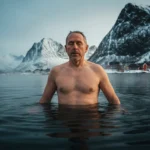 Mann står i kaldt fjordvann i Lofoten om vinteren og puster rolig