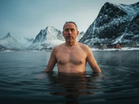 Mann står i kaldt fjordvann i Lofoten om vinteren og puster rolig