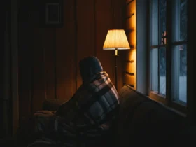 Person pakket inn i pledd i sofaen kjenner vinterdvale følelsen ved et mørkt vindu