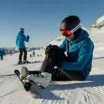 Skiløper sitter i snøen og undersøker kneet etter vintersport skader i alpinbakken
